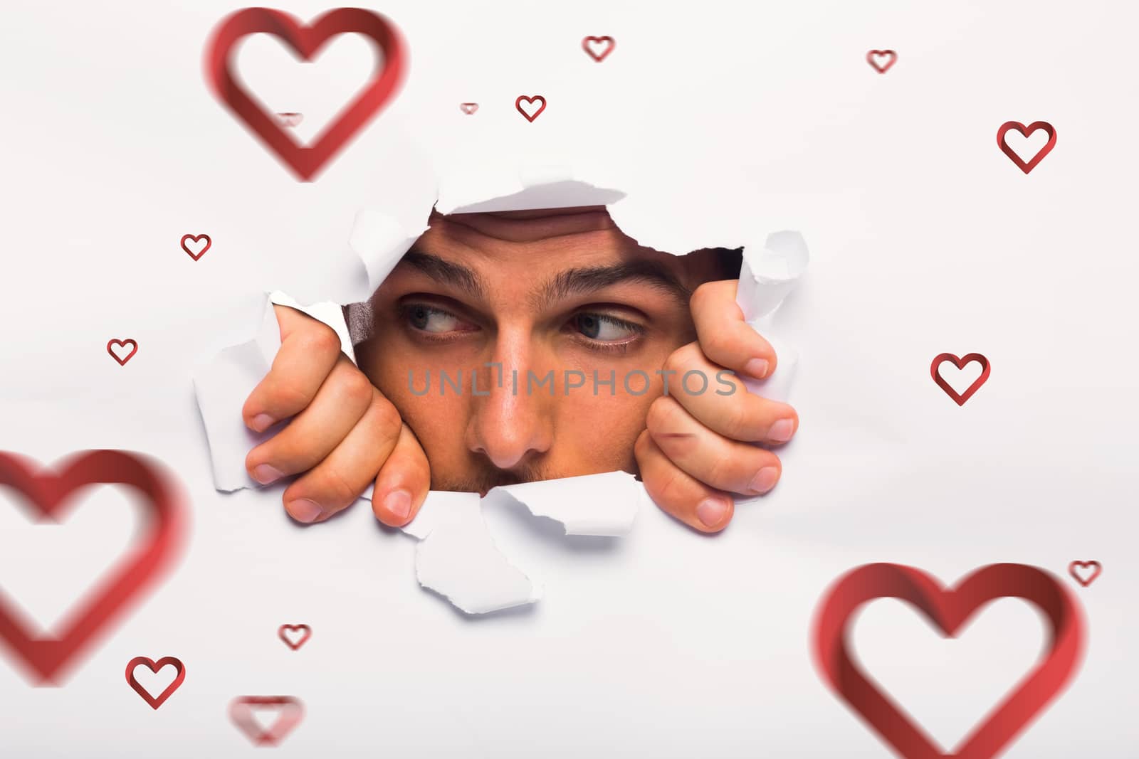Young man looking through paper rip against hearts