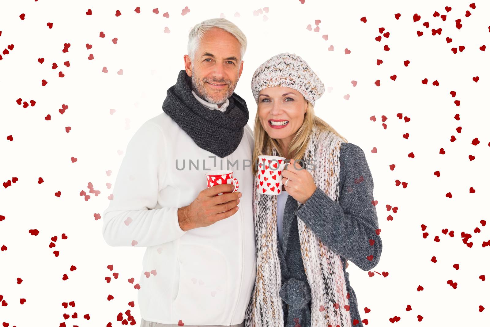 Happy couple in winter fashion holding mugs against red love hearts