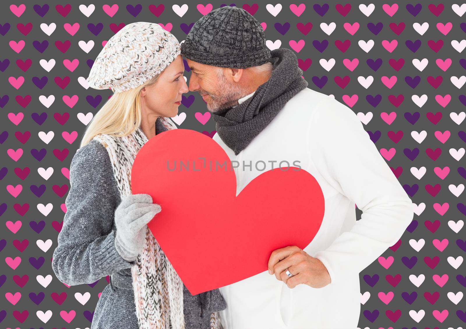 Smiling couple in winter fashion posing with heart shape against valentines day pattern