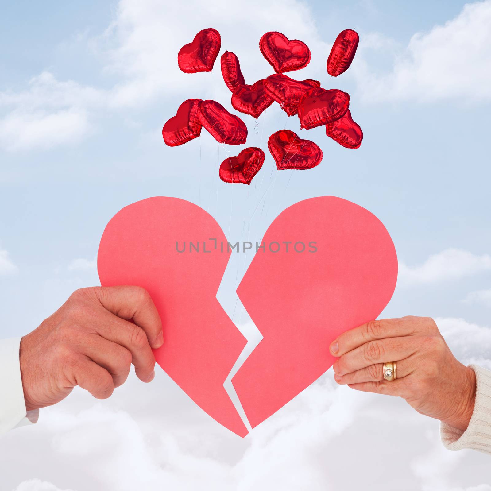 Couple holding a broken paper heart against cloudy sky