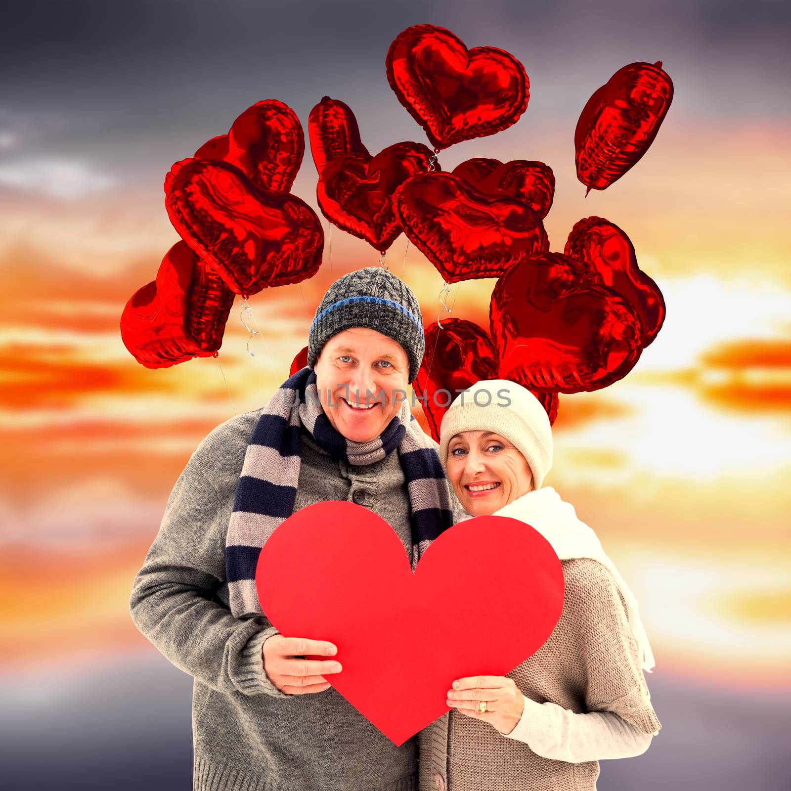 Composite image of happy mature couple in winter clothes holding red heart by Wavebreakmedia