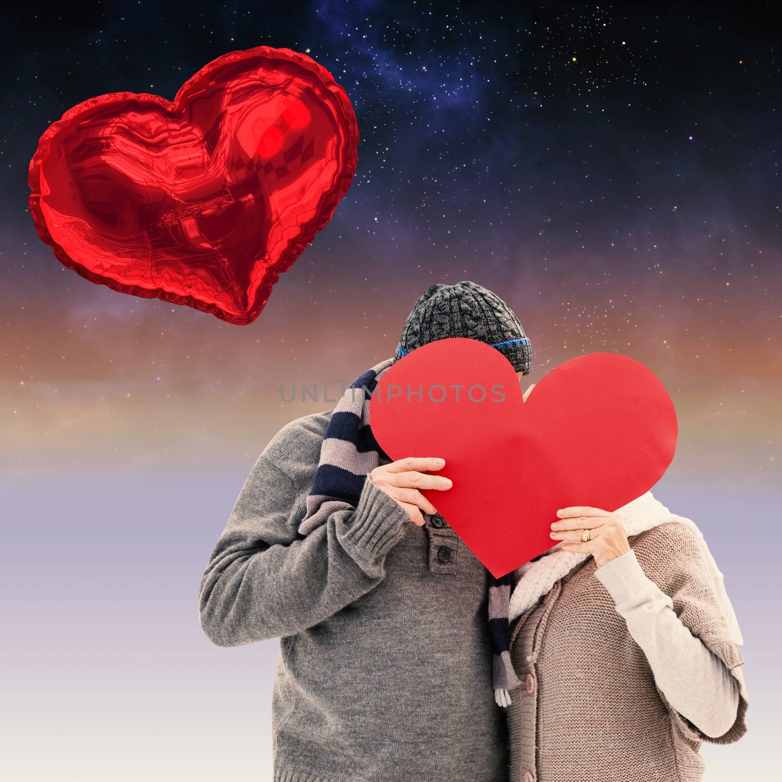 Happy mature couple in winter clothes holding red heart against aurora in night sky