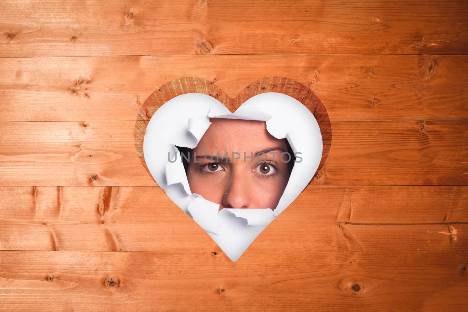Young woman looking through paper rip against heart in wood