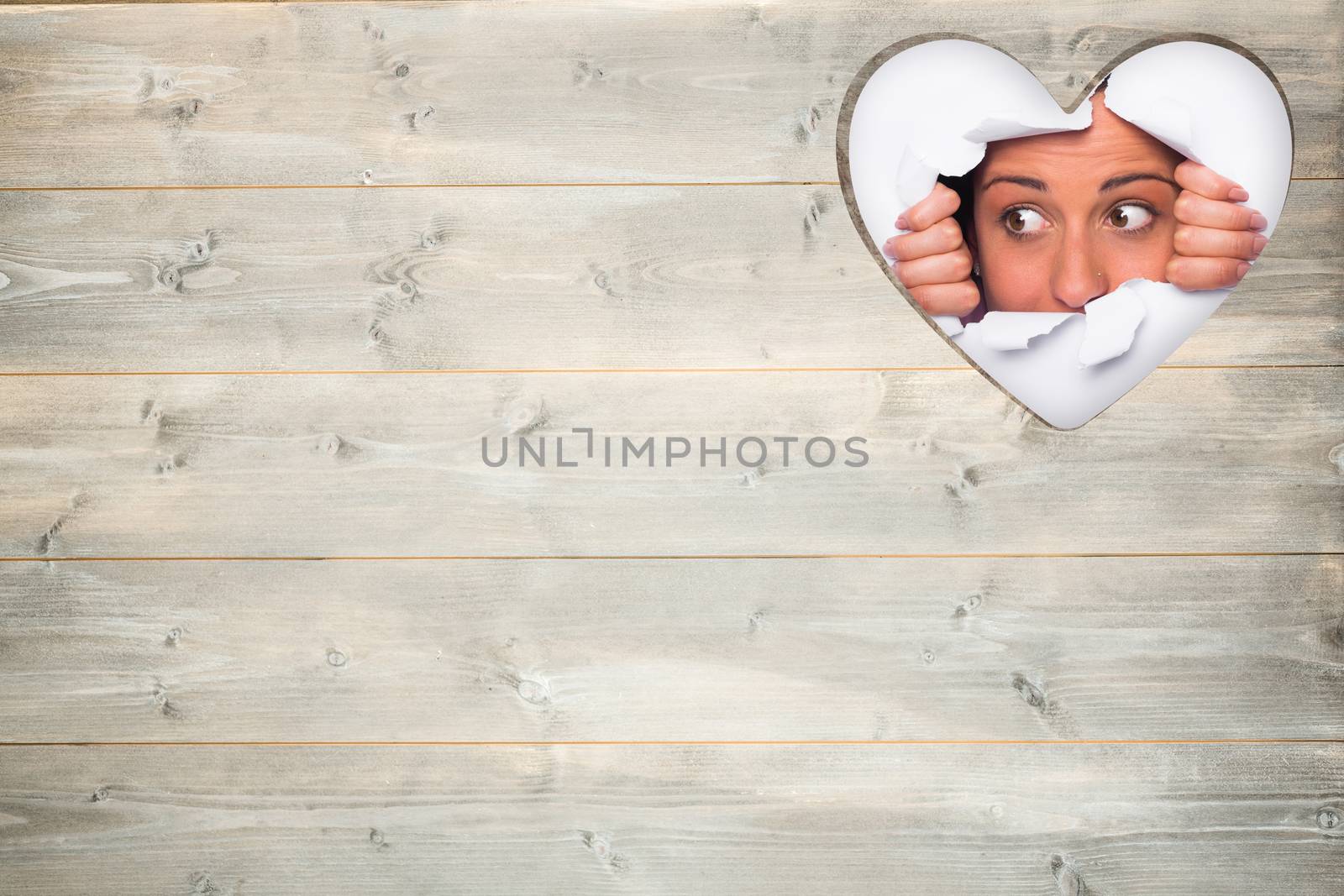 Young woman looking through paper rip against heart in wood