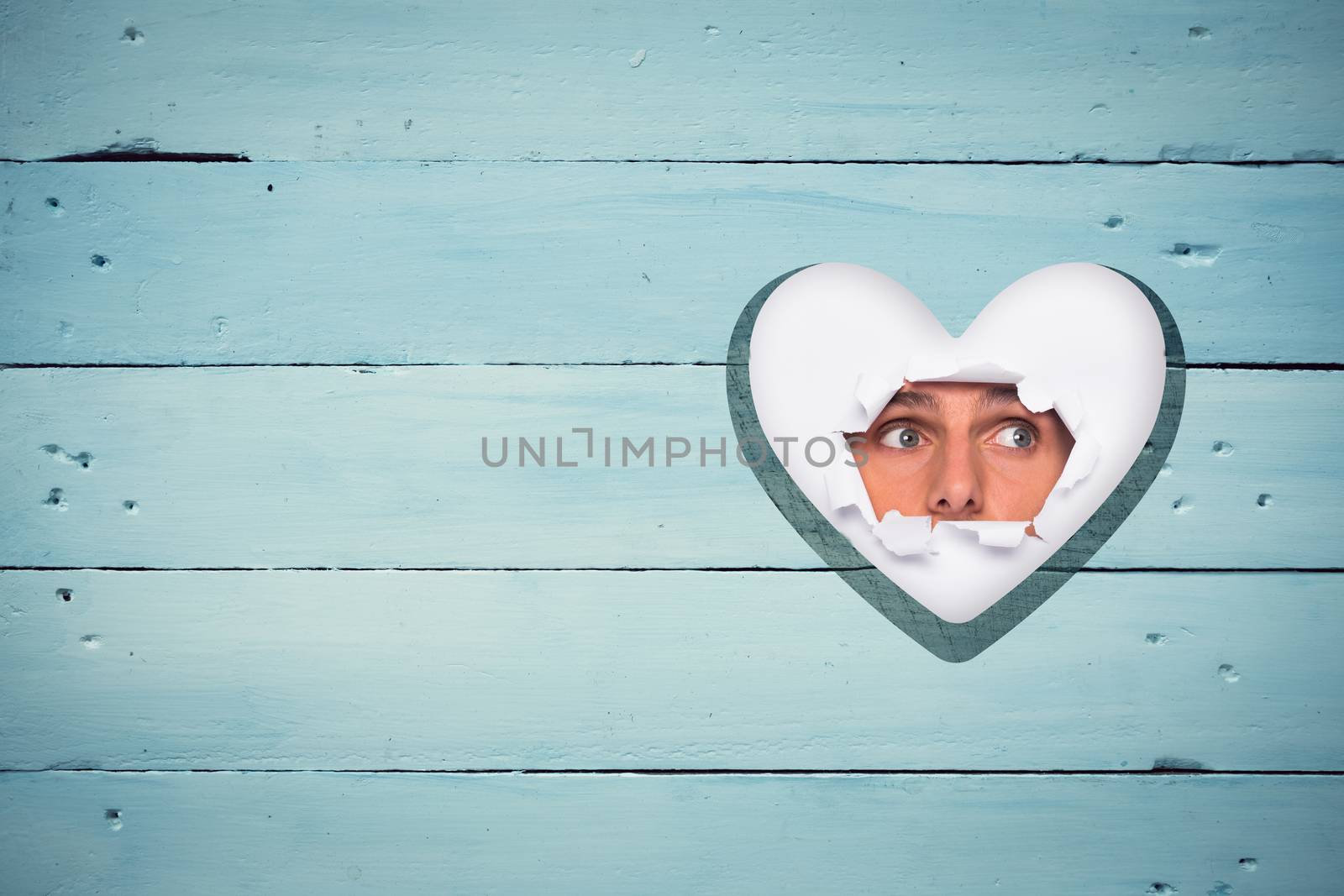 Young man looking through paper rip against heart in wood