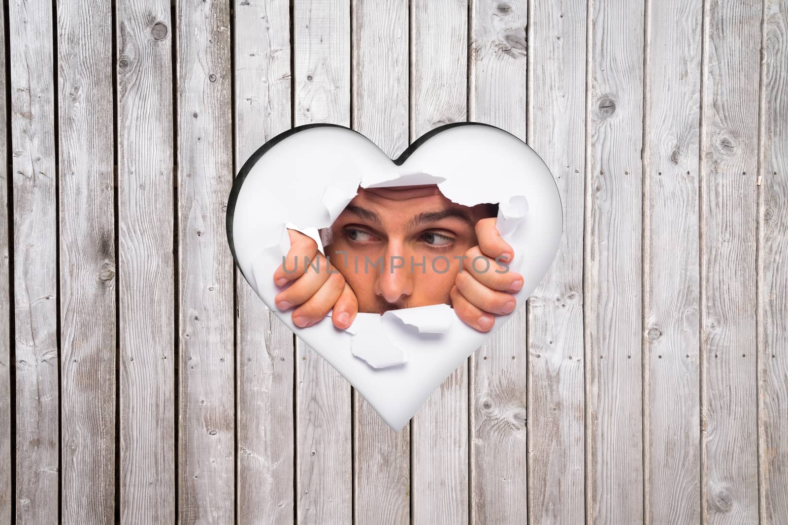 Young man looking through paper rip against heart in wood