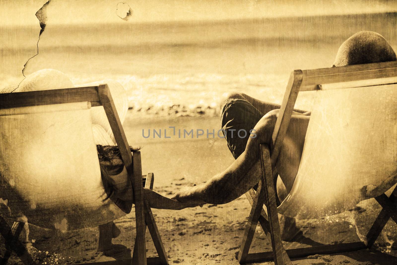 Cute couple holding hands while lying on their deck chairs against grey background