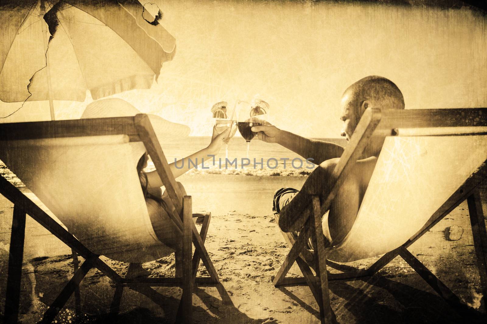 Happy couple clinking their glasses while relaxing on their deck chairs against grey background