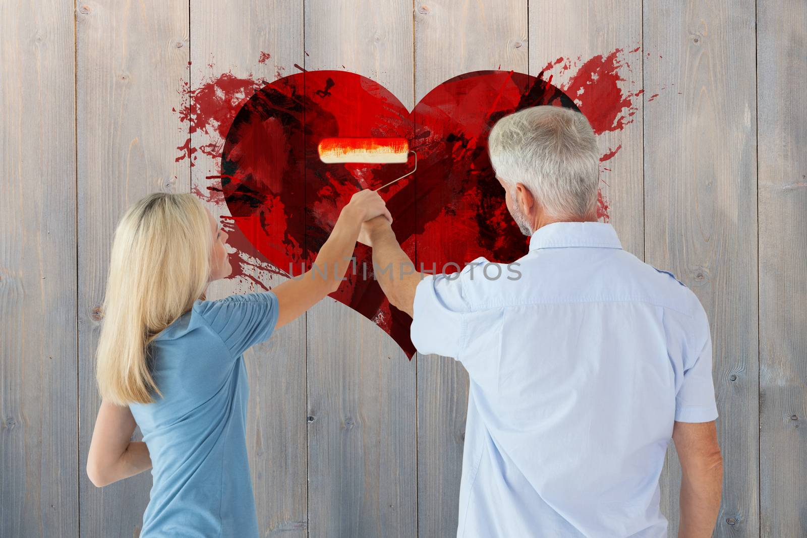 Happy couple painting wall with roller against pale grey wooden planks