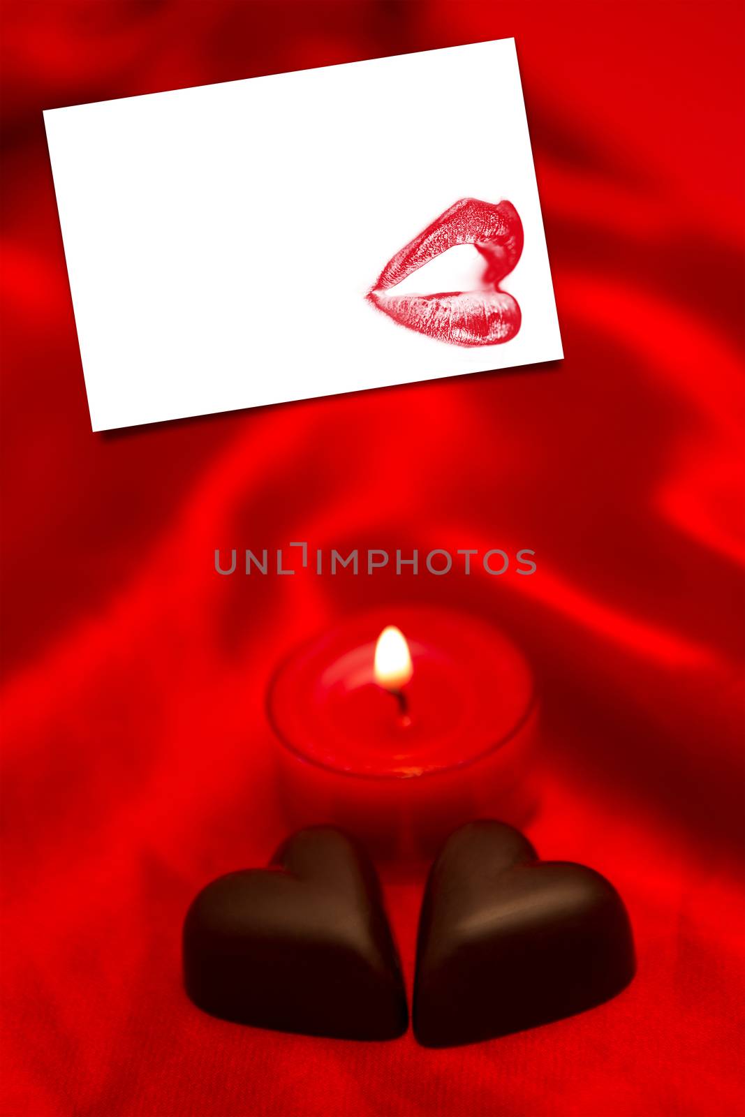 Chocolate hearts and lit candle against white card