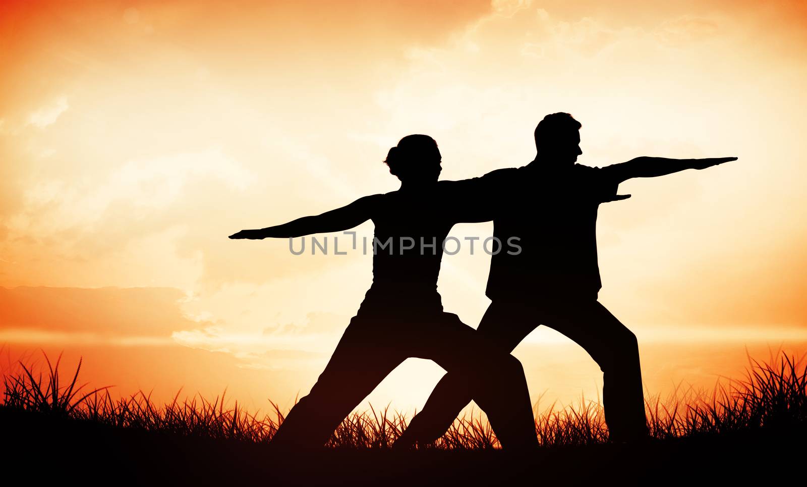 Peaceful couple in white doing yoga together in warrior position against orange sunrise
