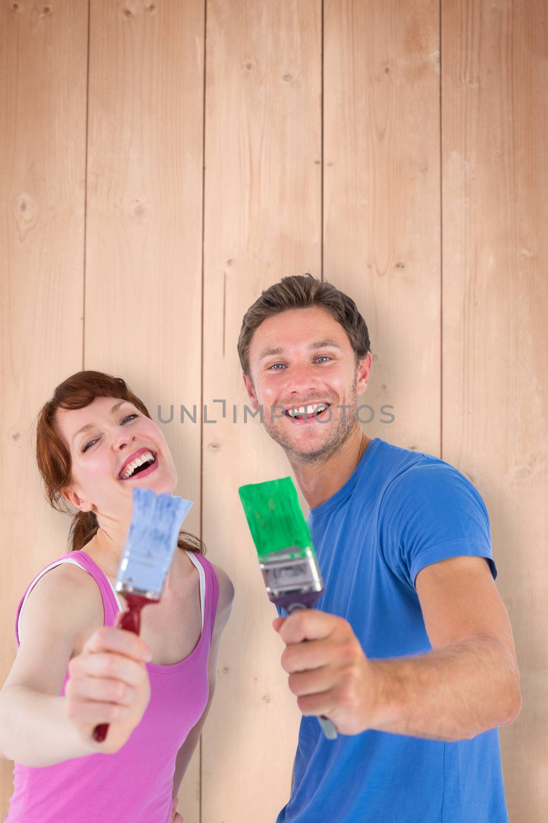 Couple both holding paint brushes against overhead of wooden planks