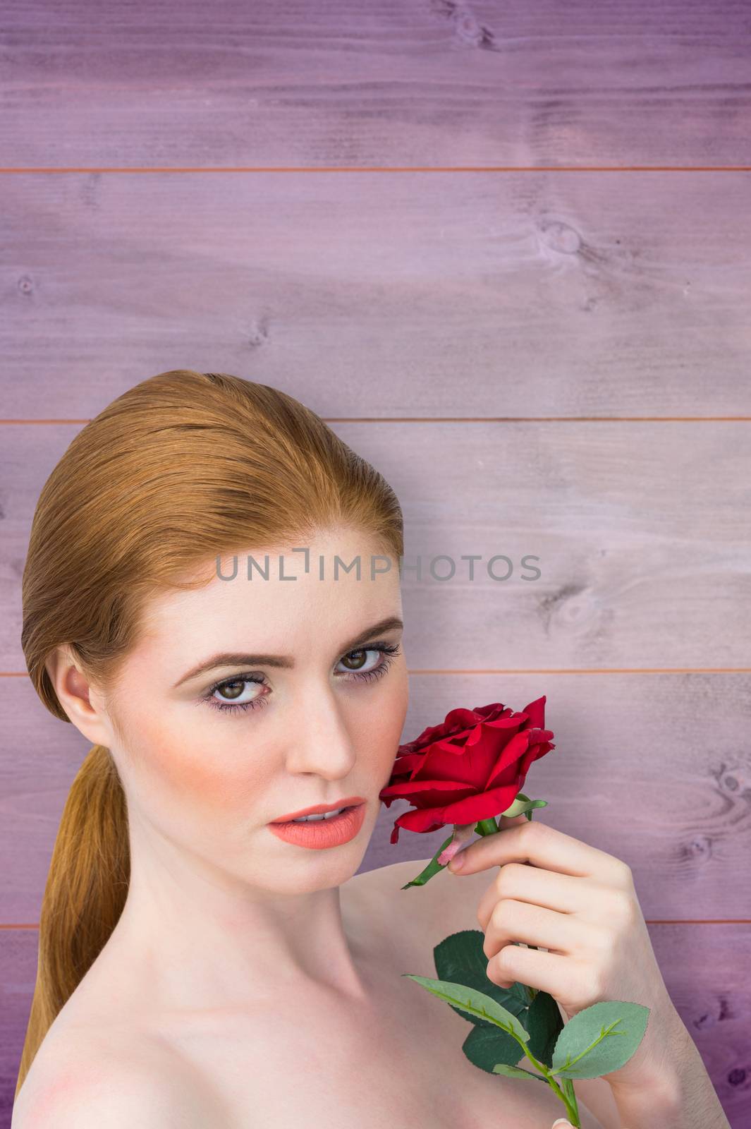 Beautiful redhead posing with red rose against wooden background in purple