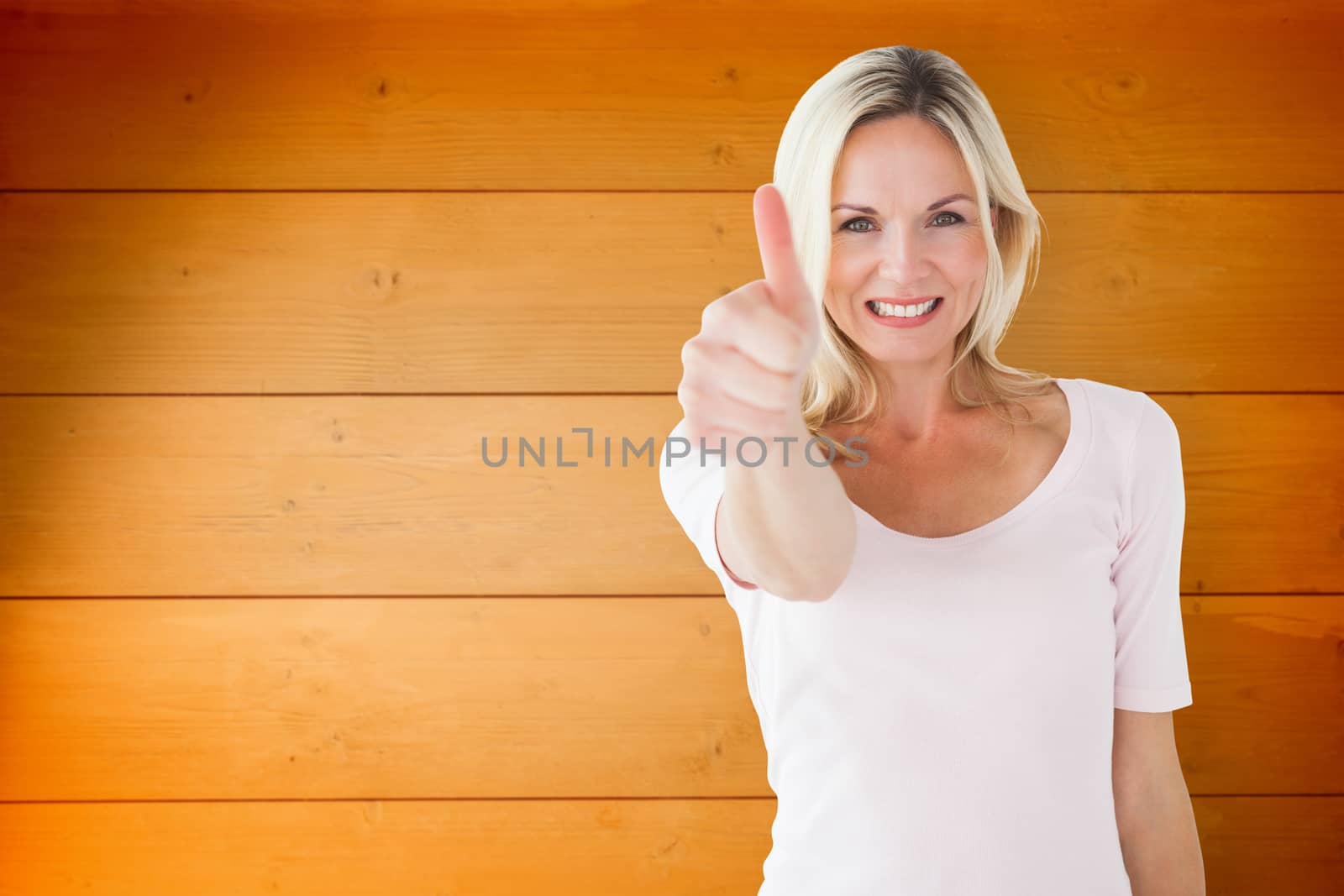 Happy blonde showing thumbs up and smiling at camera against wooden planks background