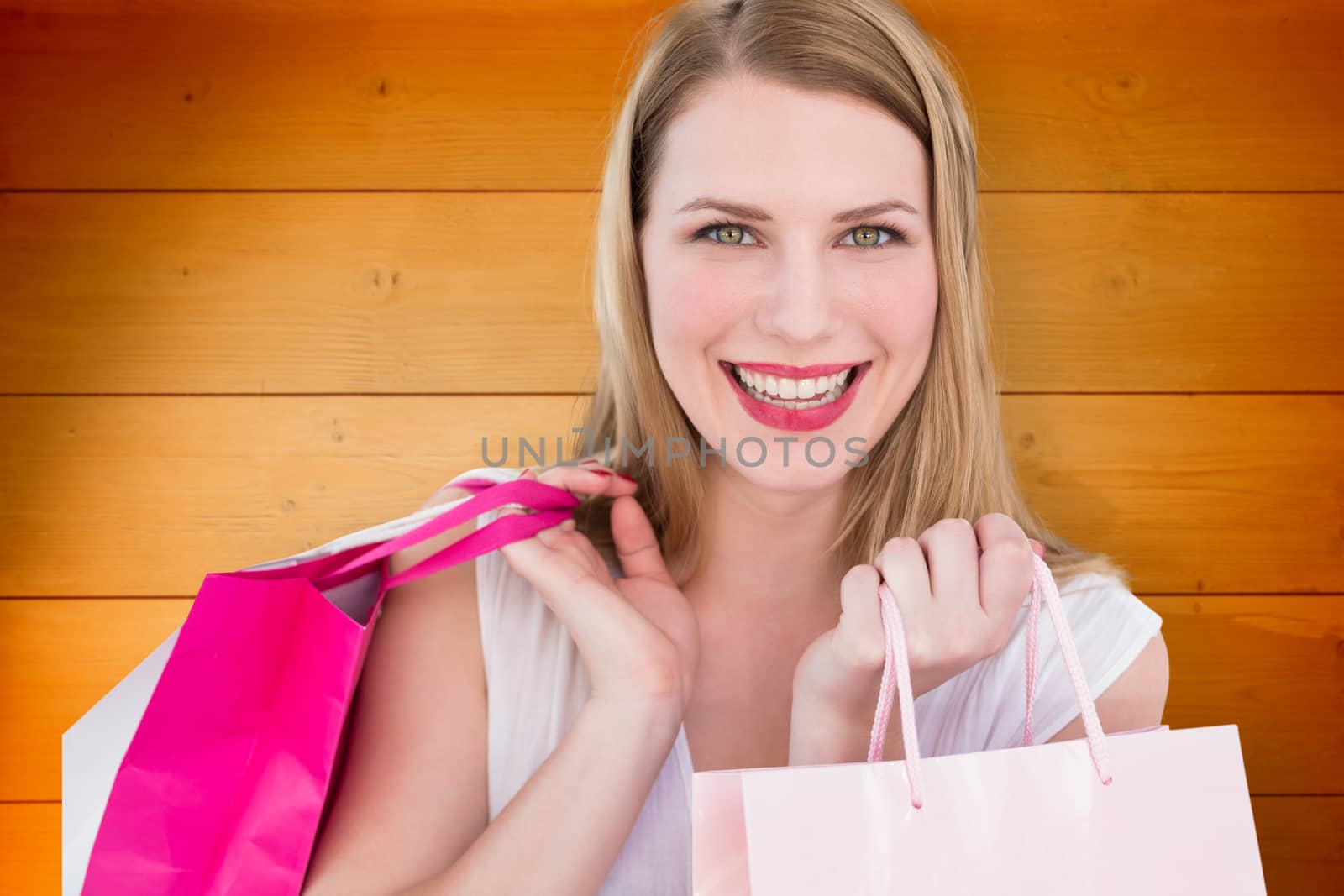 Portrait of a smiling blonde woman holding shopping bags against wooden planks background