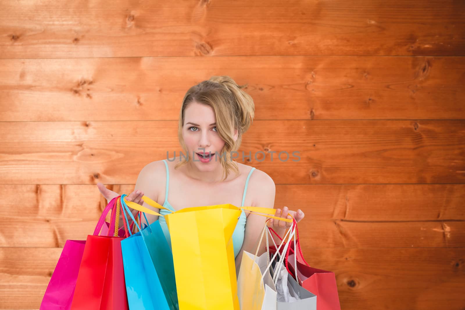 Excited woman looking at camera with many shopping bags against overhead of wooden planks