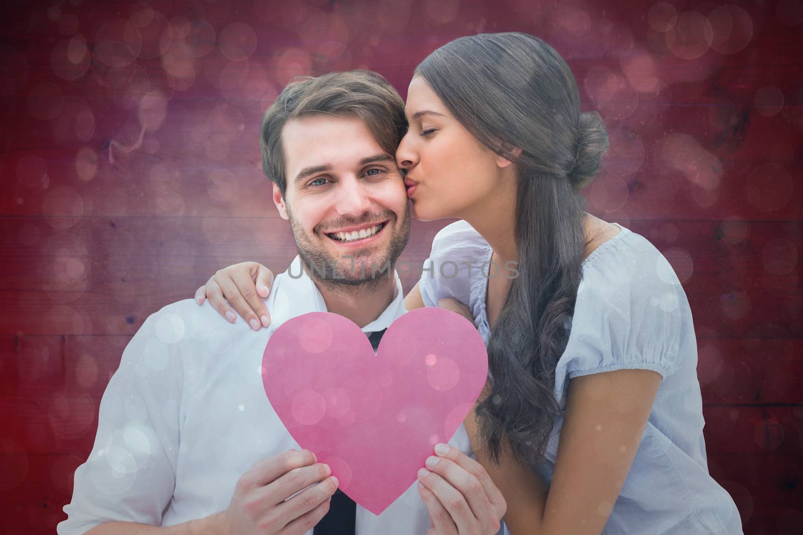 Pretty brunette giving boyfriend a kiss and her heart against blue abstract light spot design