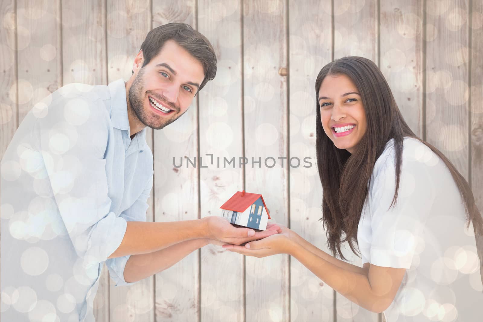 Attractive young couple holding a model house against light glowing dots design pattern