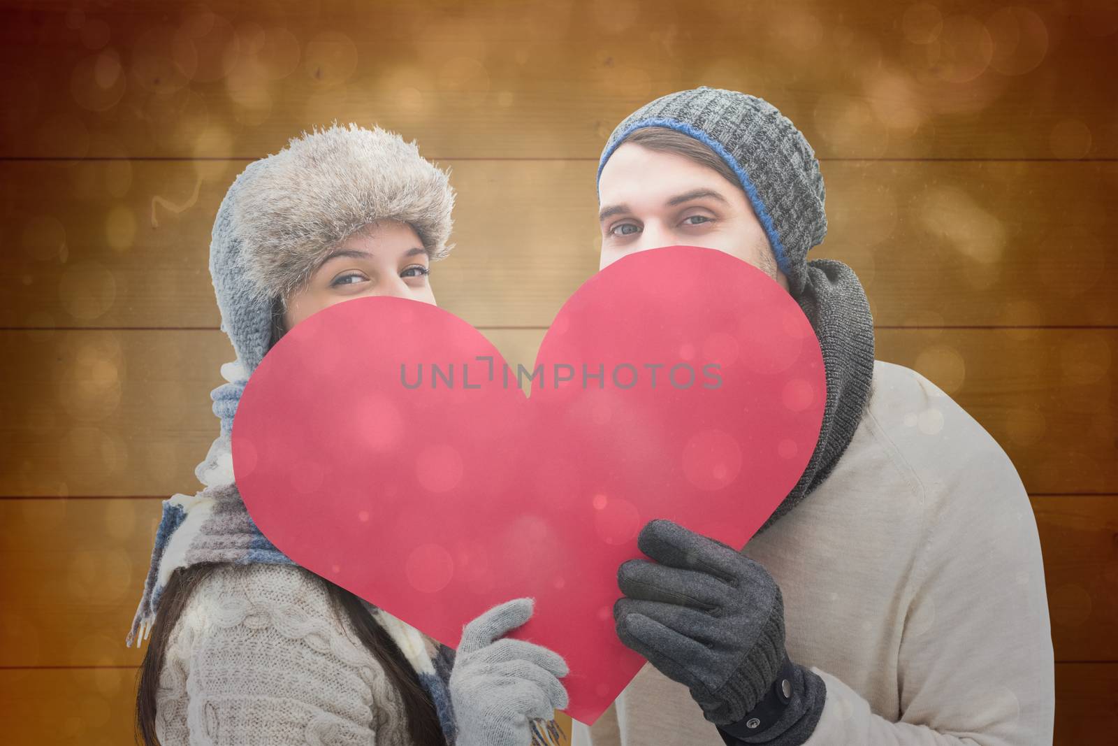 Composite image of attractive young couple in warm clothes holding red heart by Wavebreakmedia