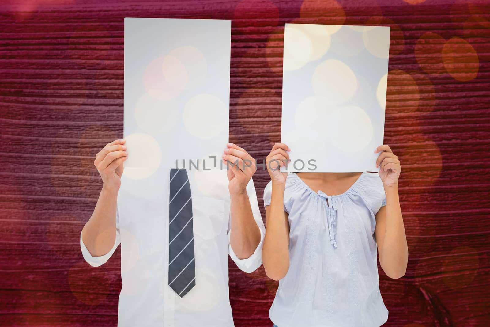 Couple holding paper over their faces against close up of christmas lights