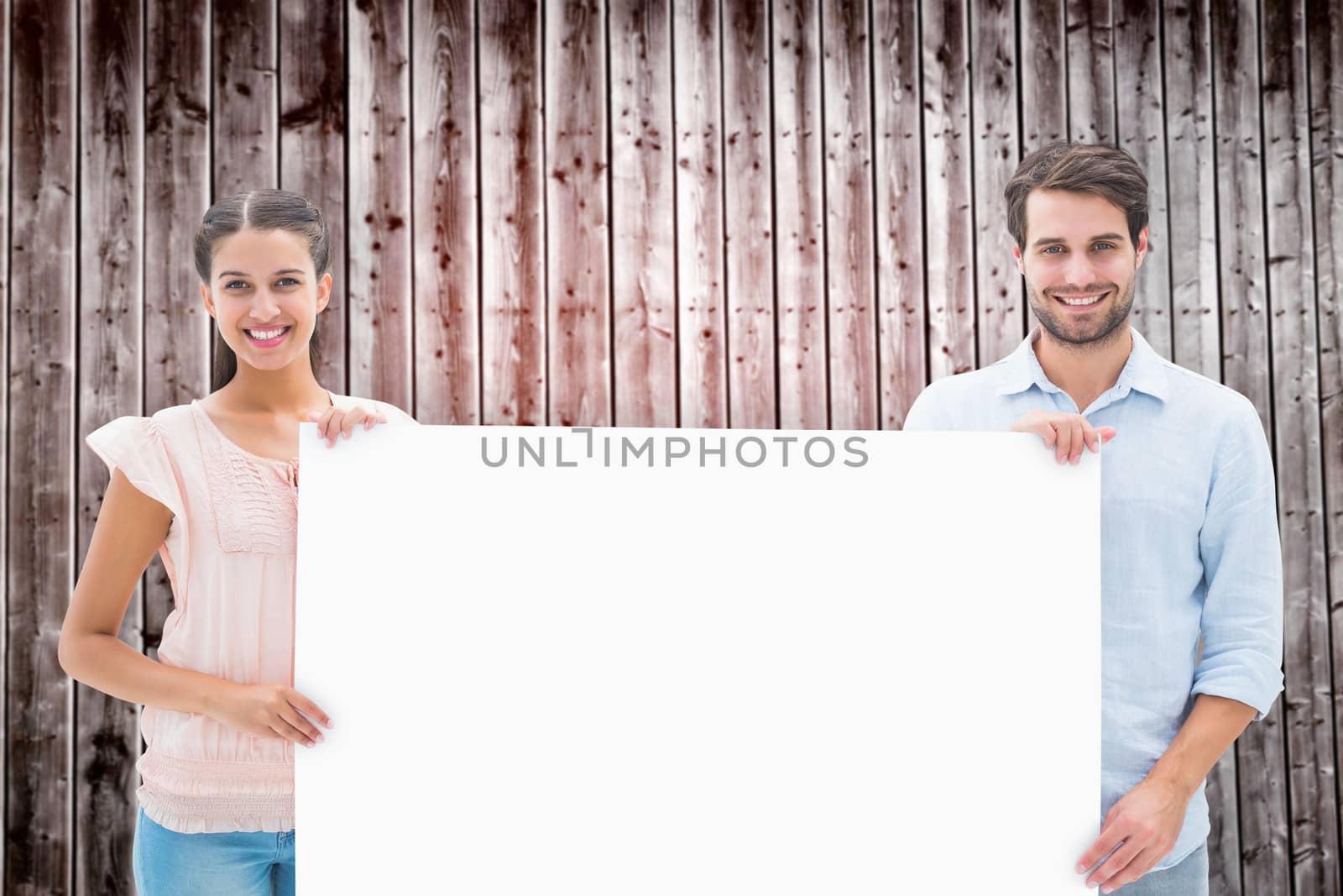 Attractive young couple smiling at camera holding poster against wooden planks