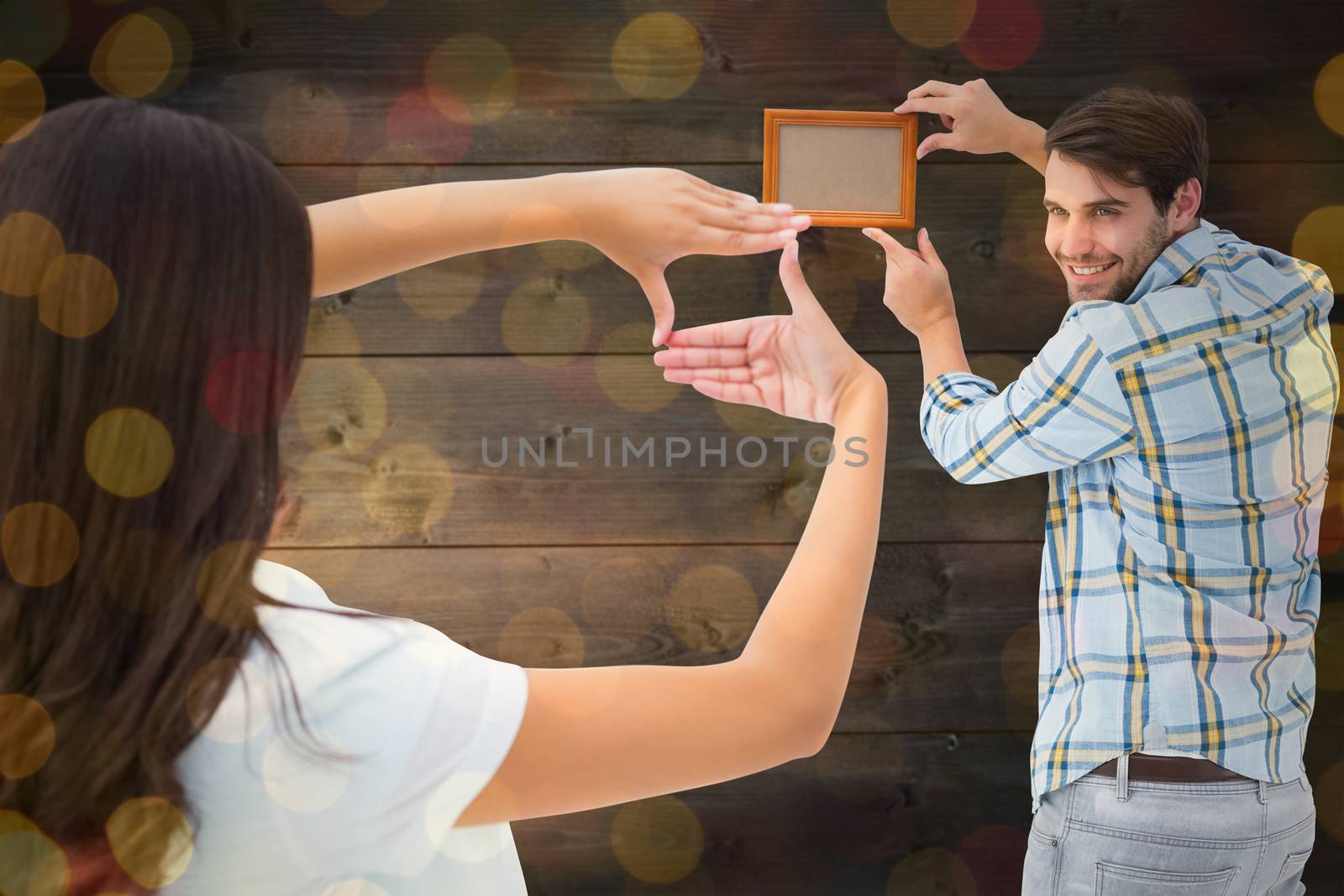 Happy young couple putting up picture frame against close up of christmas lights