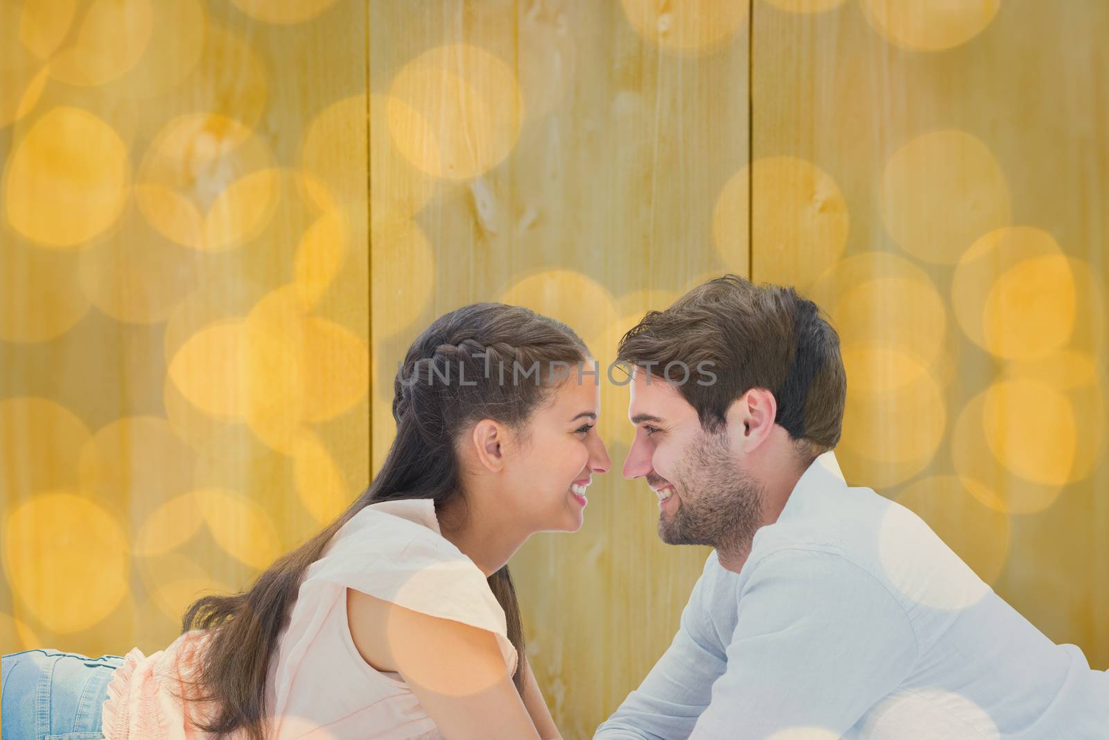 Attractive young couple smiling at each other against blurry yellow christmas light circles