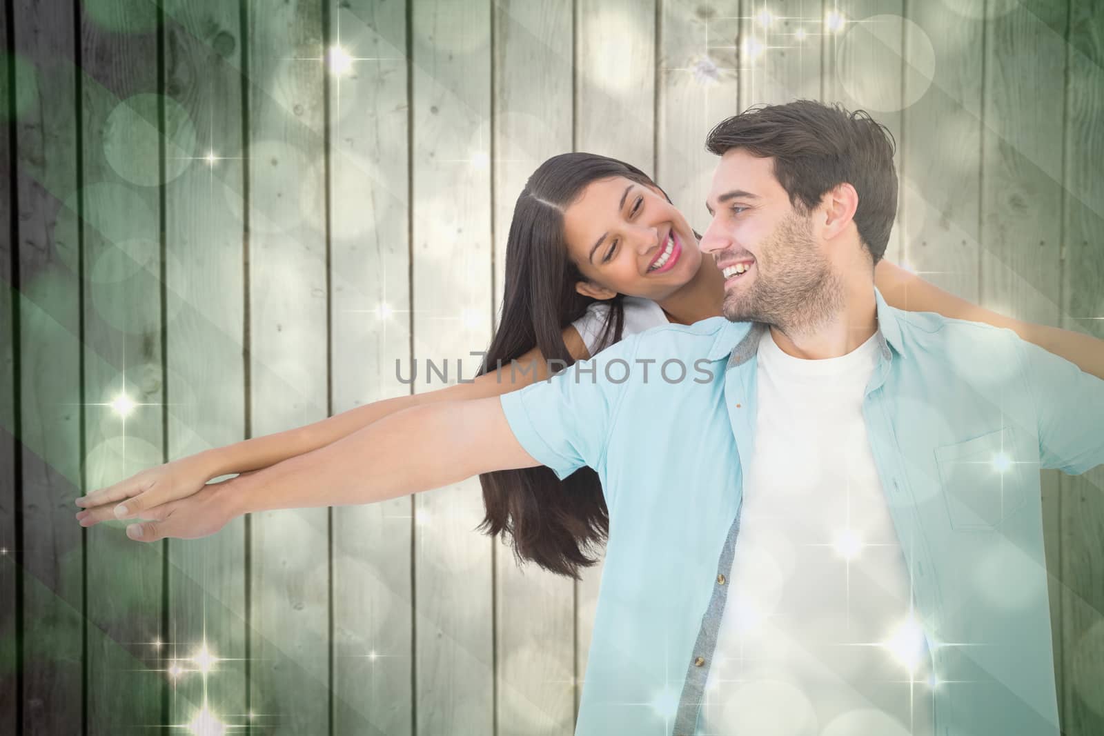 Happy casual man giving pretty girlfriend piggy back against light design shimmering on green