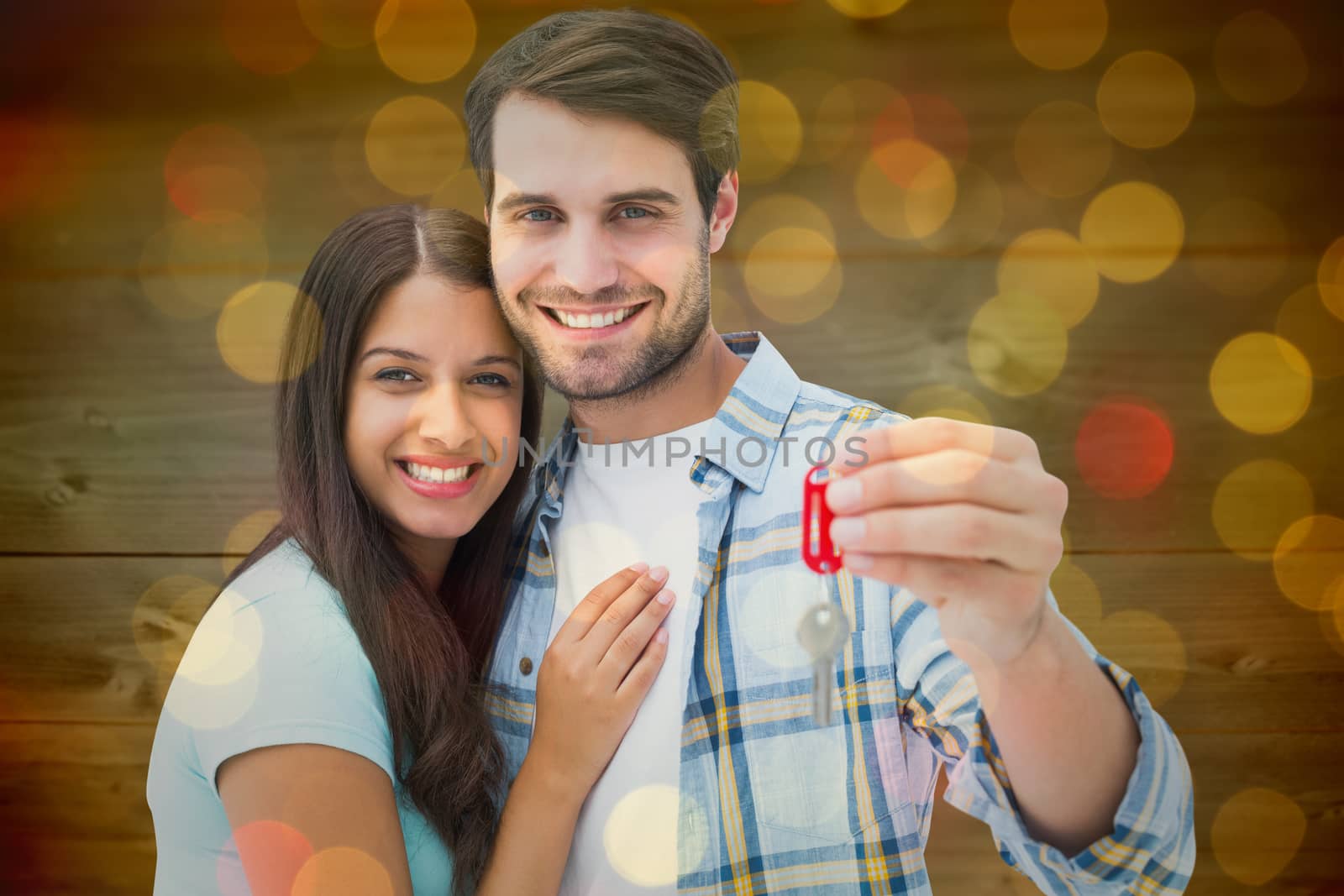 Happy young couple holding new house key against close up of christmas lights