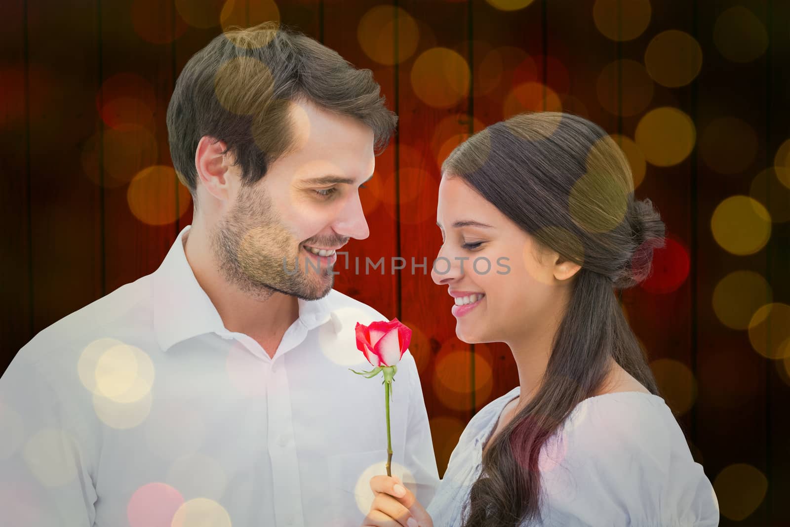 Handsome man offering his girlfriend a rose against close up of christmas lights