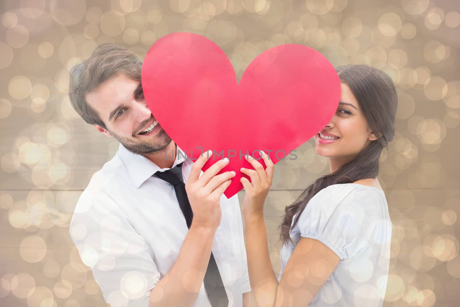Couple smiling at camera holding a heart against light glowing dots design pattern