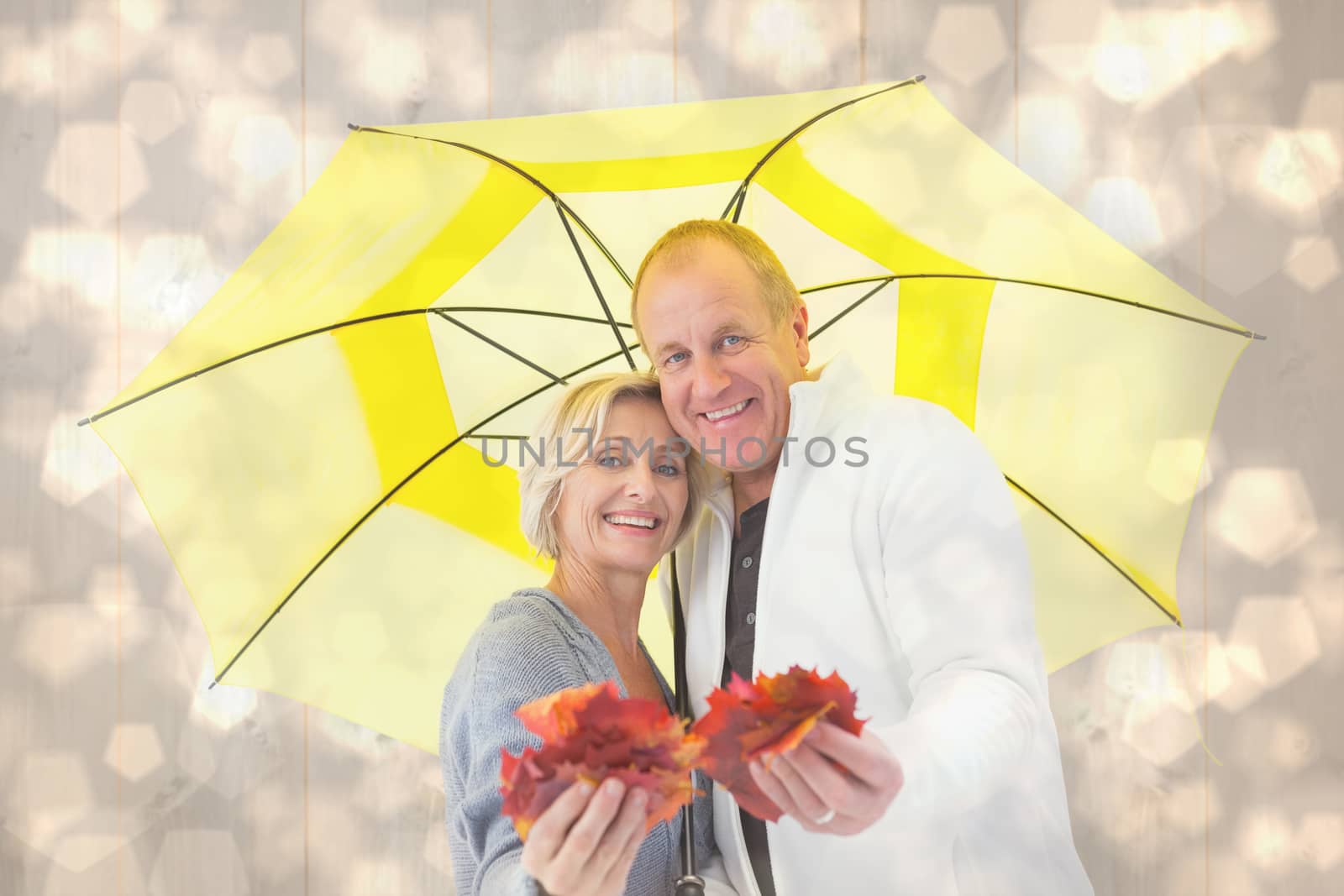 Happy mature couple showing autumn leaves under umbrella against light glowing dots design pattern