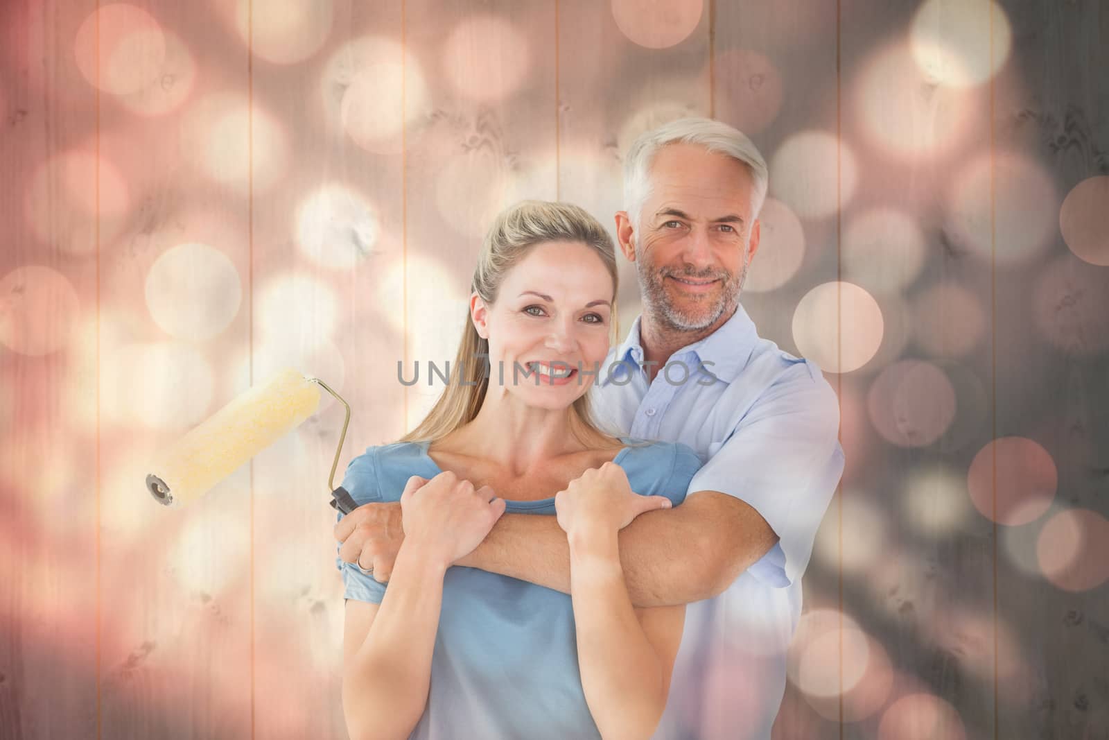 Happy couple hugging and holding paint roller against light circles on black background