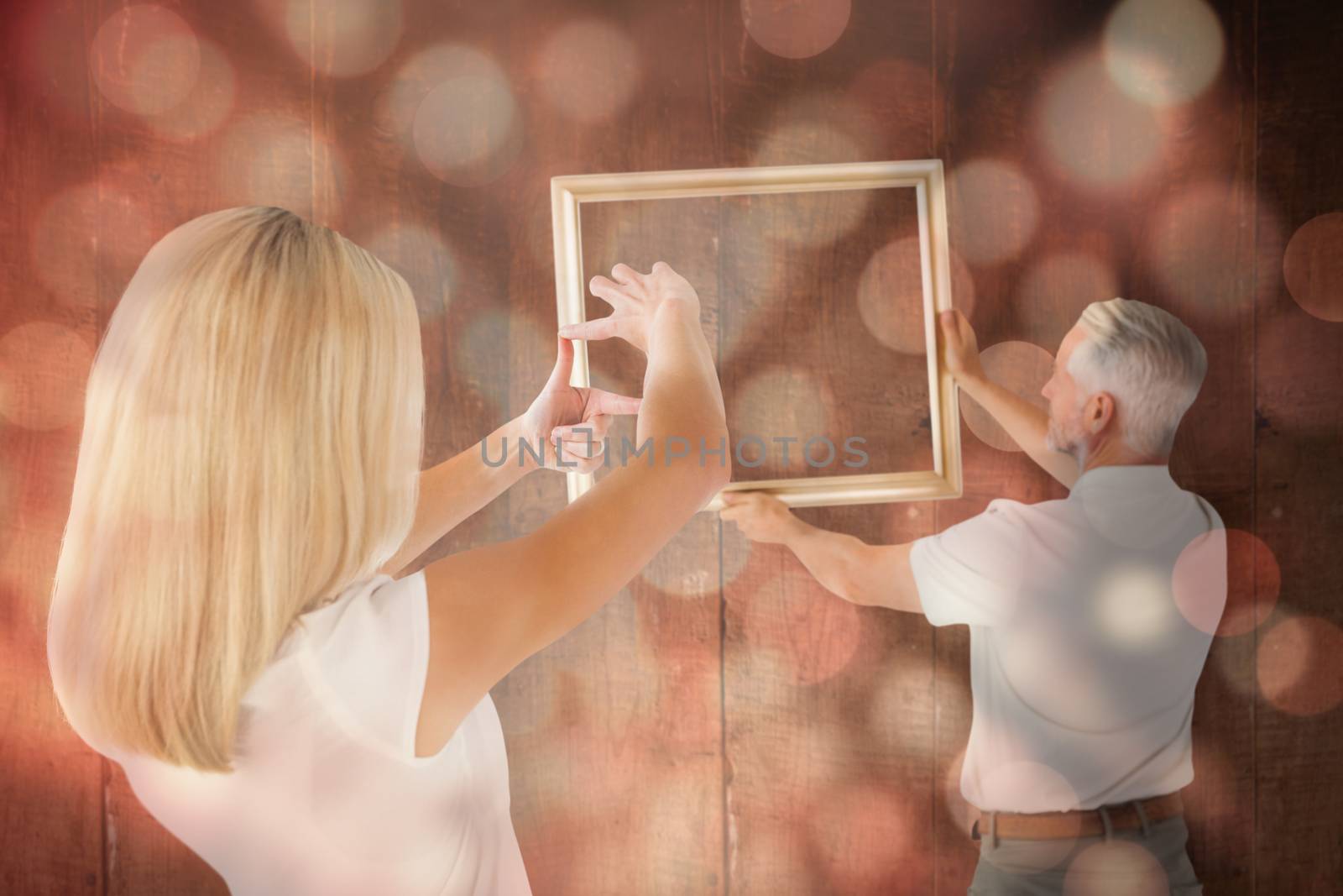 Composite image of couple hanging a frame together by Wavebreakmedia