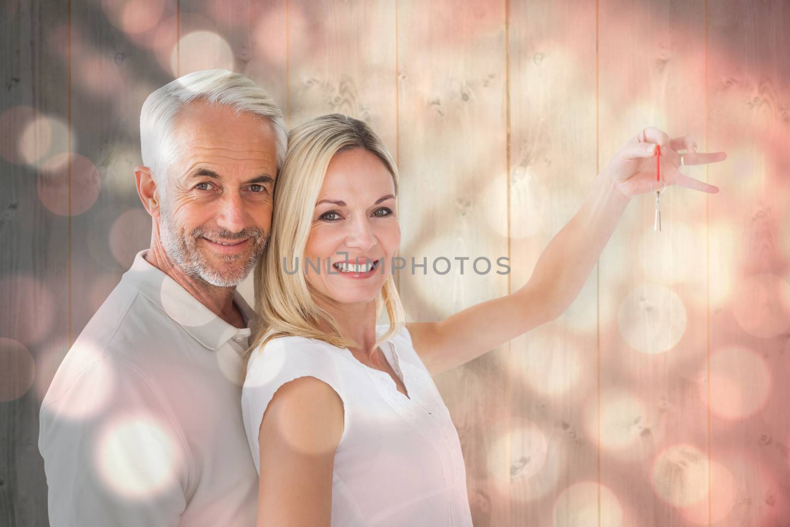 Happy couple showing their new house key against light circles on black background
