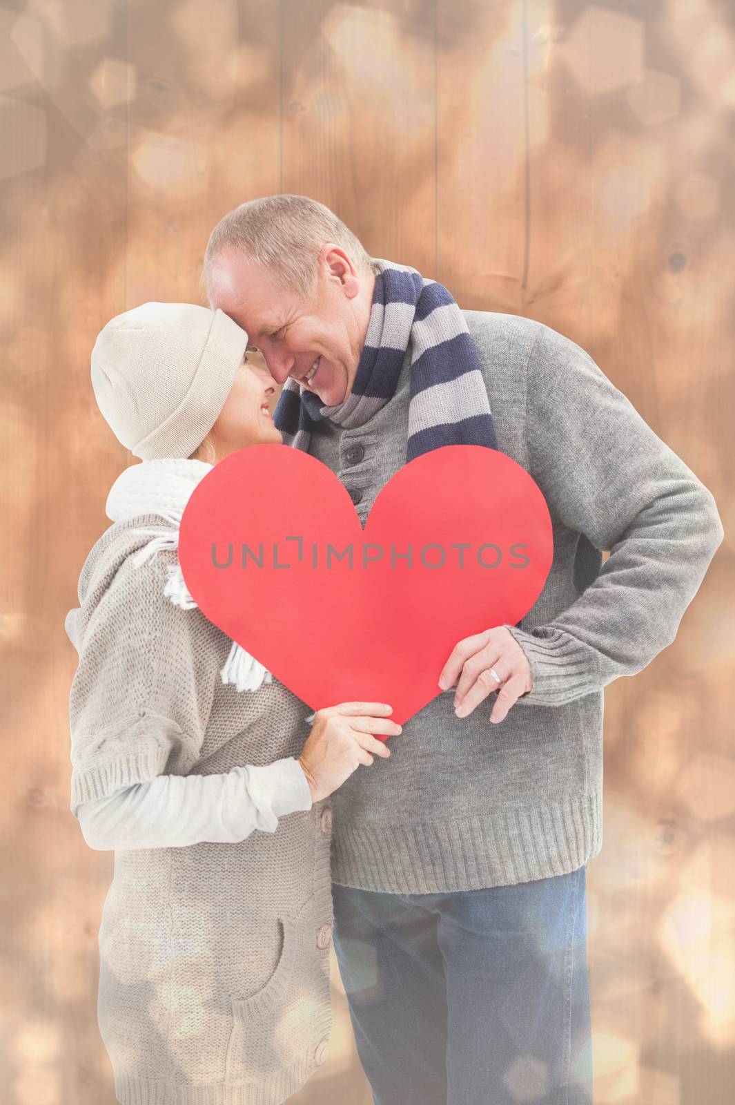 Happy mature couple in winter clothes holding red heart against light glowing dots design pattern