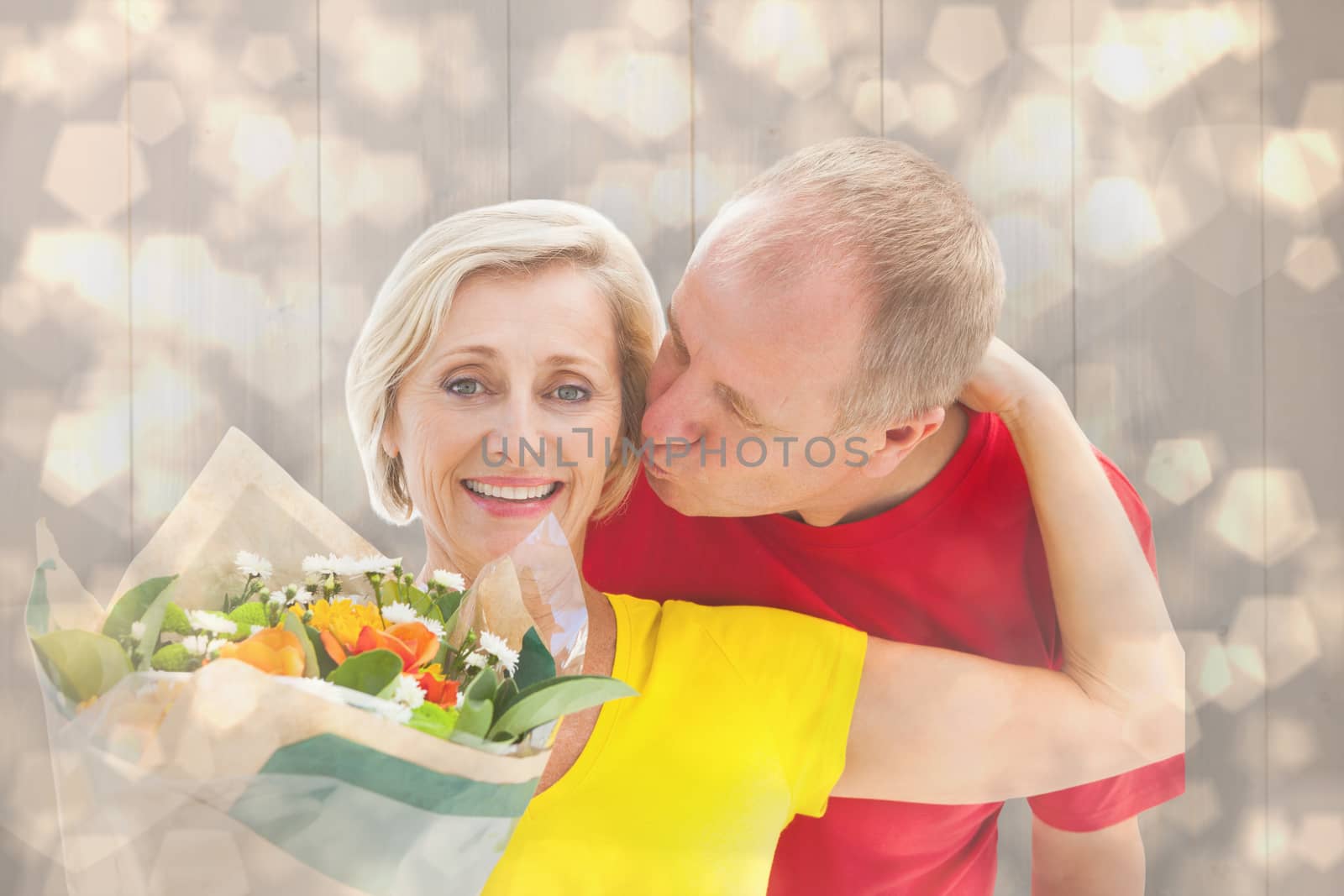 Mature man kissing his partner holding flowers against light glowing dots design pattern