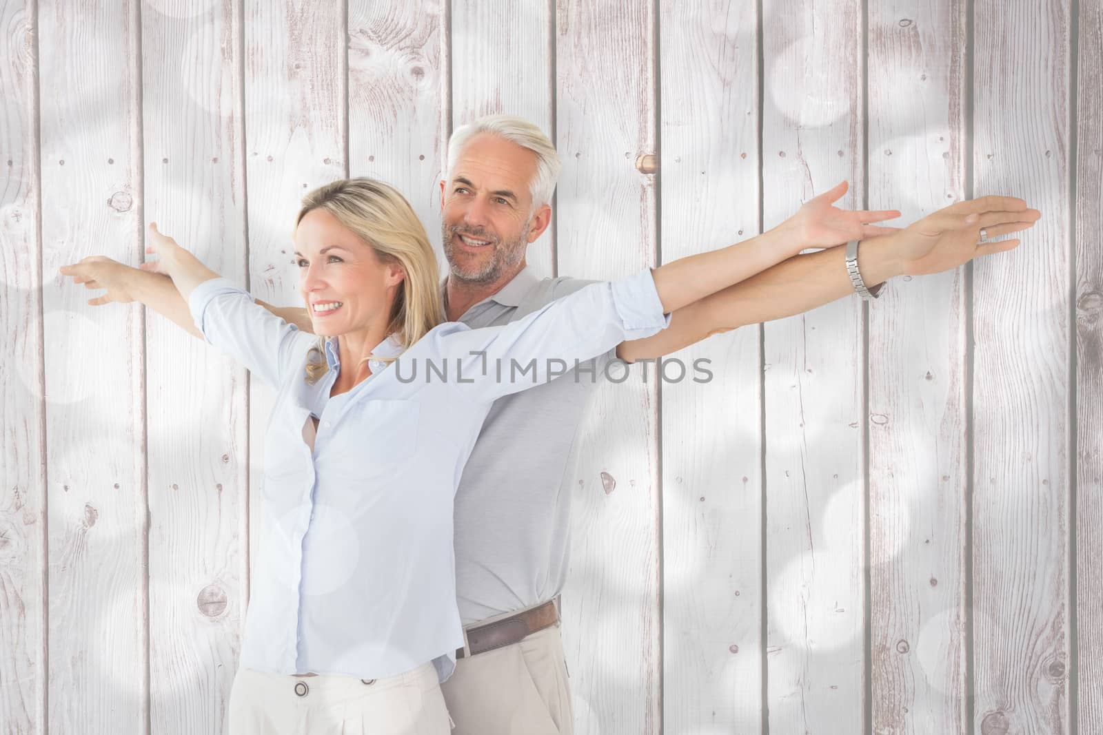 Composite image of happy couple standing with arms outstretched by Wavebreakmedia