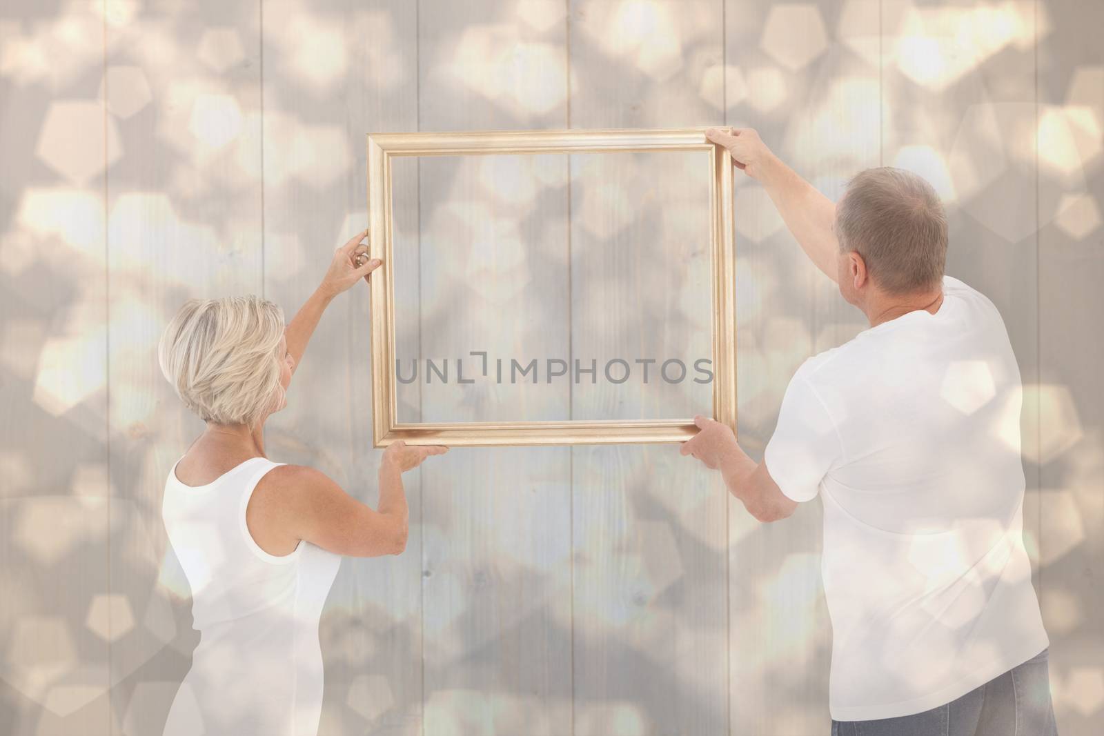 Mature couple hanging up picture frame against light glowing dots design pattern