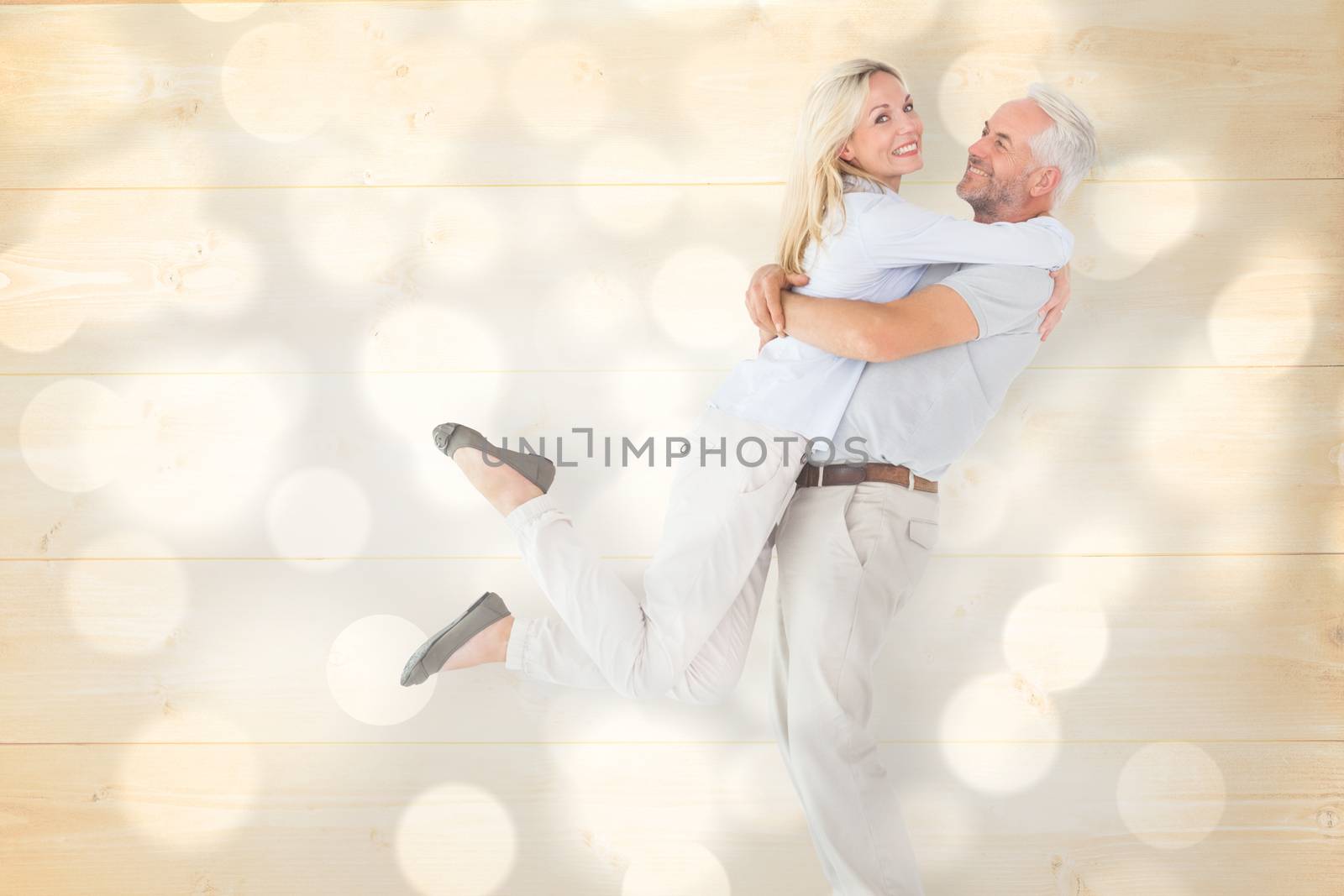 Man picking up his partner while hugging here against light circles on grey background