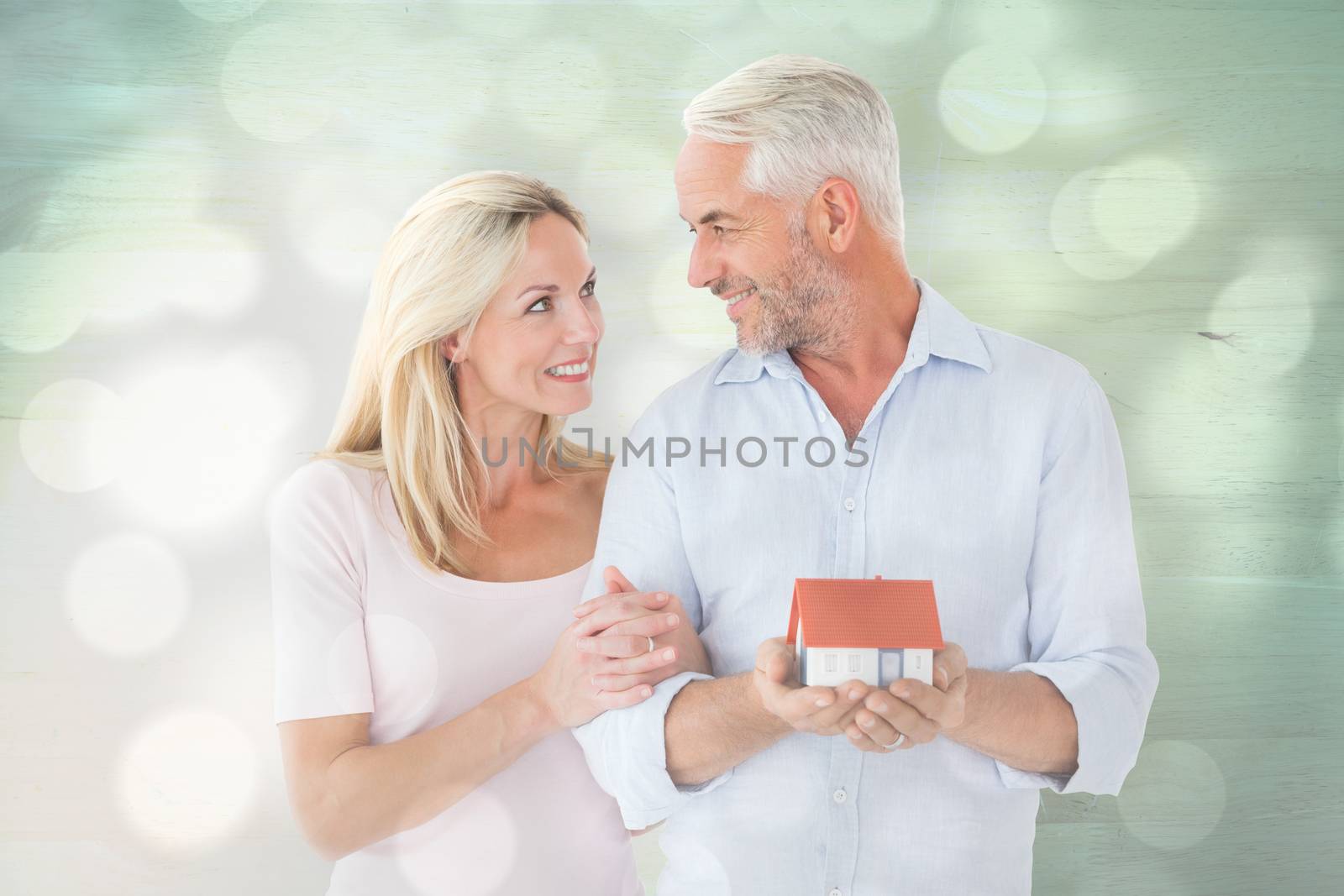 Happy couple holding miniature model house against light circles on grey background