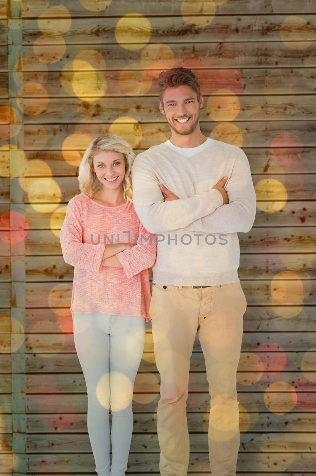 Attractive couple smiling with arms crossed against close up of christmas lights