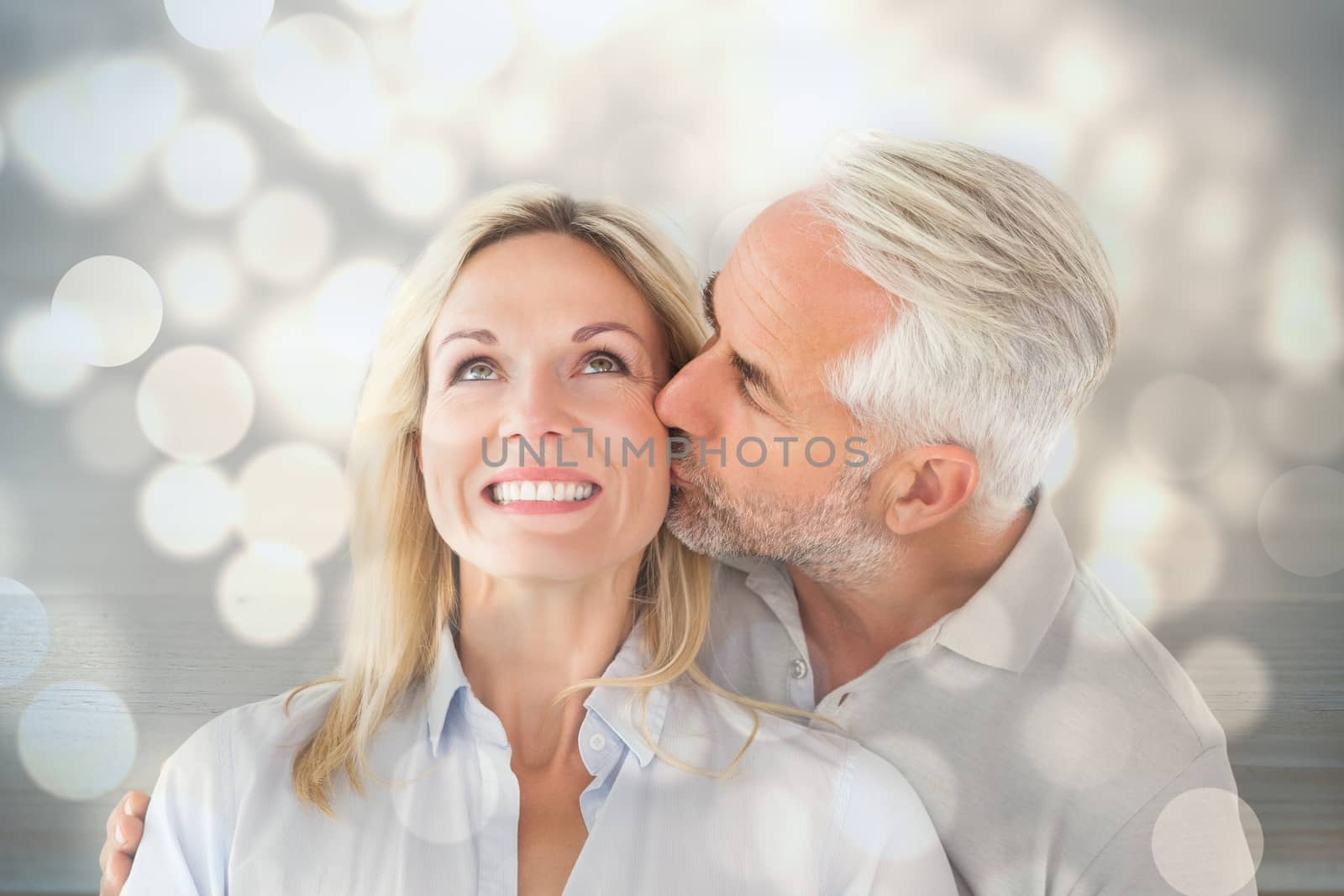 Affectionate man kissing his wife on the cheek  against light circles on bright background