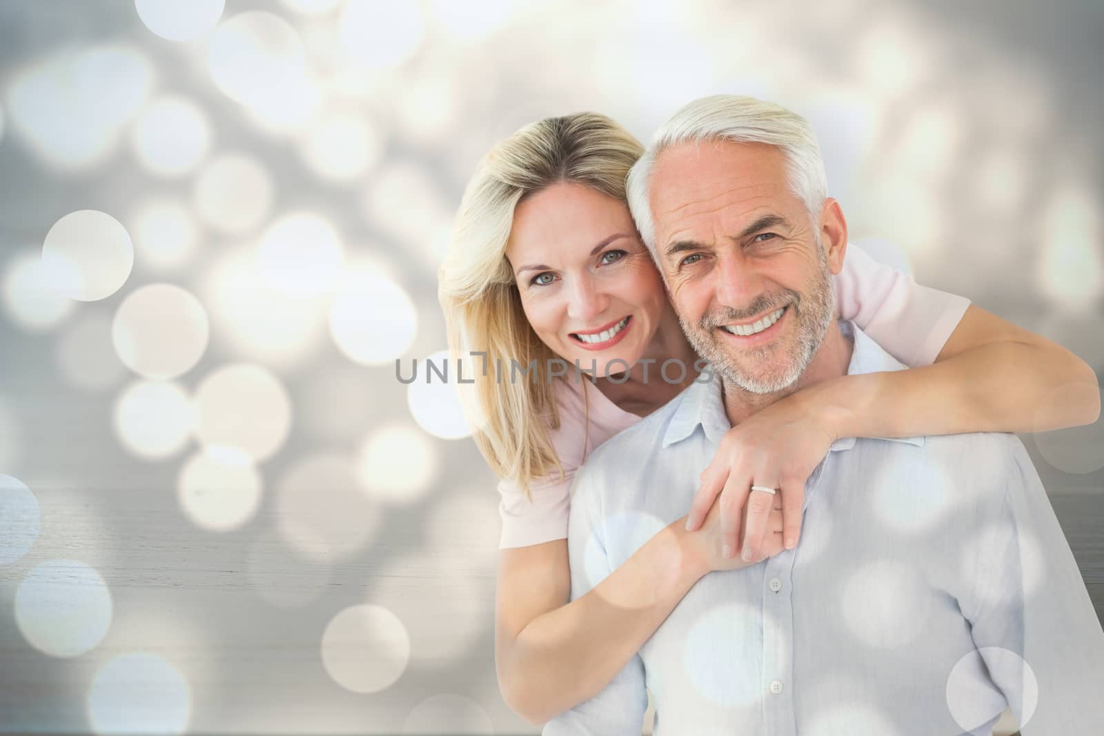 Smiling couple embracing and looking at camera against light circles on bright background