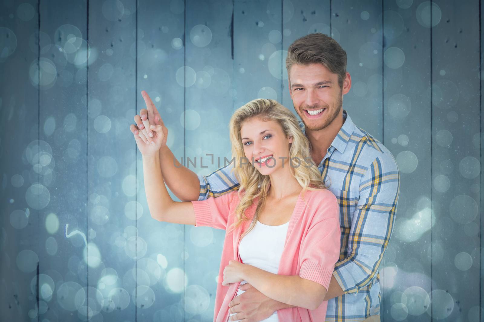 Attractive young couple embracing and pointing  against blue abstract light spot design