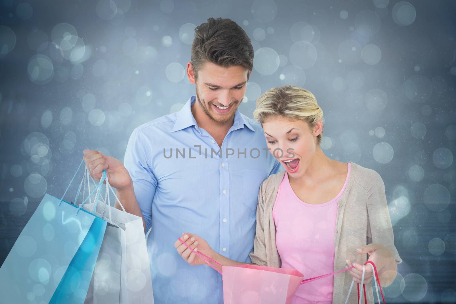 Attractive young couple holding shopping bags against blue abstract light spot design