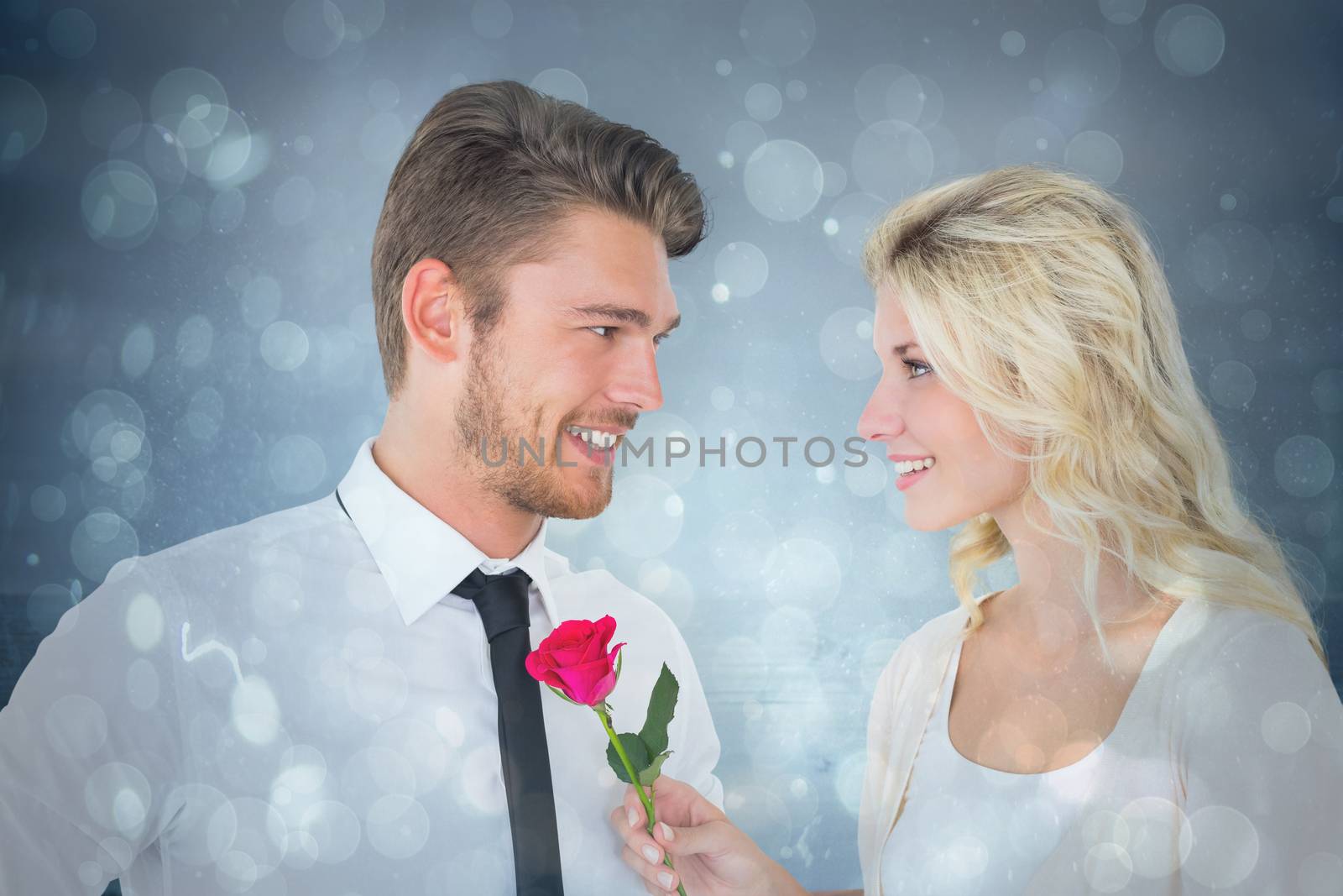 Handsome man smiling at girlfriend holding a rose against blue abstract light spot design
