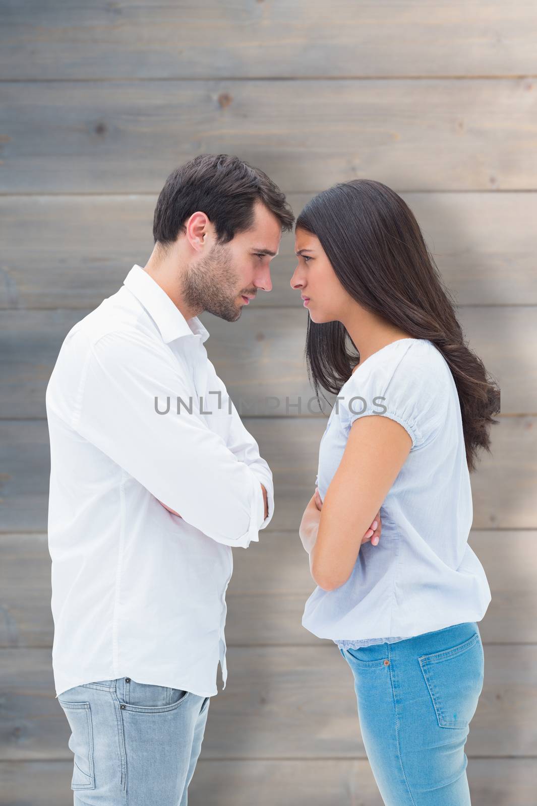 Angry couple facing off after argument against pale grey wooden planks