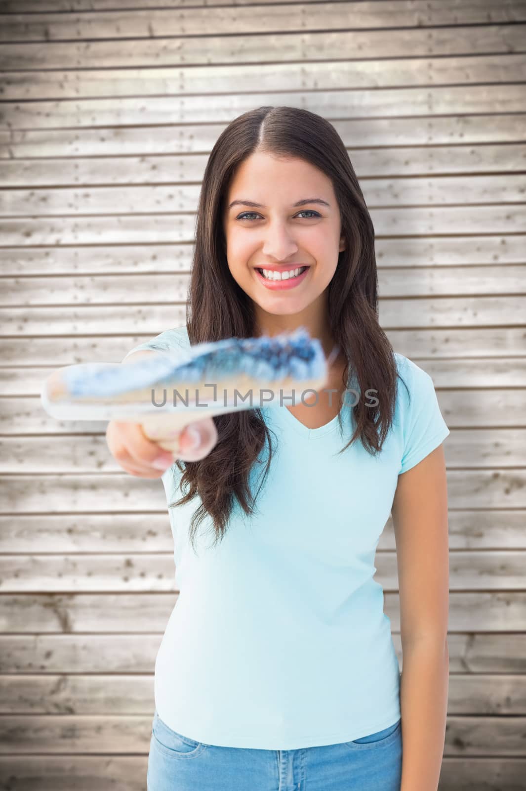 Happy young brunette holding paintbrush against wooden planks background