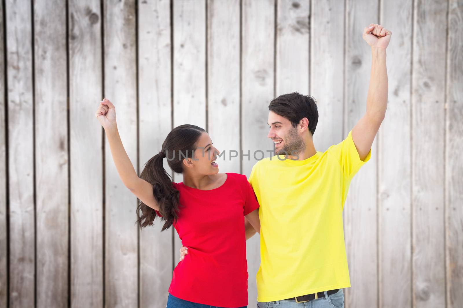 Excited couple cheering in red and yellow tshirts against wooden planks